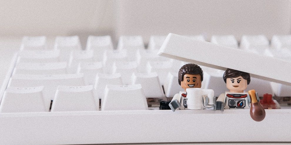 Dos minifiguras LEGO asoman entre las teclas de un teclado con una taza de café